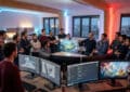 Diverse French game developers collaborate in a modern studio, viewing a holographic game world, code, and 3D models on screens.