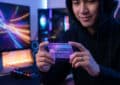 Young gamer with subtle smile holds a glowing, translucent 'Game Credit Voucher' card in a modern, ambiently lit gaming setup.