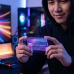 Young gamer with subtle smile holds a glowing, translucent 'Game Credit Voucher' card in a modern, ambiently lit gaming setup.