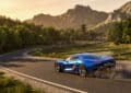 A vibrant metallic electric blue hypercar speeds on a winding road in a lush Japanese mountain landscape at golden hour, with a pagoda and torii gate.