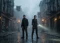 Two individuals stand alertly on a wet, foggy street in a dark, decaying city at night, one with a flashlight beam.
